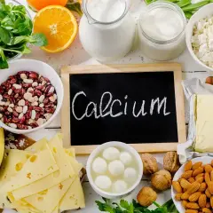 Talerzyk z serem, fasolą, orzechami, migdałami, pomarańczą i nabiałem. Na tablicy napis "Calcium".