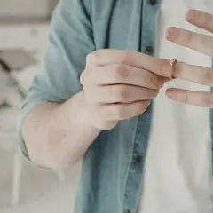Mężczyzna zdejmuje obrączkę, symbolizując złamane serce. W tle siedzi smutna kobieta.