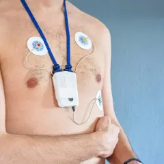 Mężczyzna z przyklejonymi elektrodami i urządzeniem holter ekg na klatce piersiowej, monitorującym pracę serca.