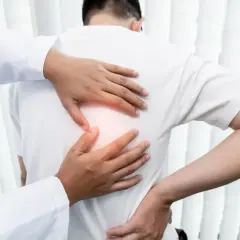 Lekarz bada pacjenta z bólem pod lewą łopatką. Dłonie terapeuty delikatnie dotykają pleców, wskazując na źródło dyskomfortu.