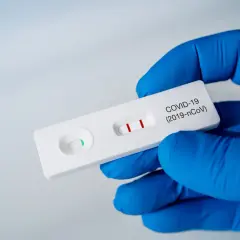 Rękawiczka w niebieskiej rękawiczce trzyma test na COVID-19 z dwoma czerwonymi paskami. Zastanawiasz się, ile kosztuje test na COVID?