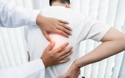 Lekarz bada pacjenta z bólem pod lewą łopatką. Dłonie terapeuty delikatnie dotykają pleców, wskazując na źródło dyskomfortu.