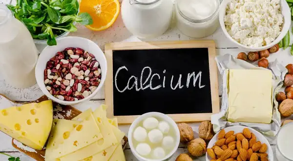Talerzyk z serem, fasolą, orzechami, migdałami, pomarańczą i nabiałem. Na tablicy napis "Calcium".