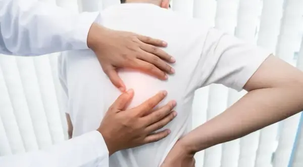 Lekarz bada pacjenta z bólem pod lewą łopatką. Dłonie terapeuty delikatnie dotykają pleców, wskazując na źródło dyskomfortu.
