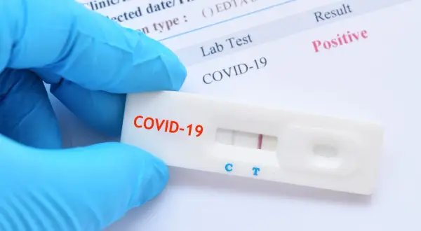 Ręka w niebieskiej rękawiczce trzyma test antygenowy COVID-19 z dwoma widocznymi paskami, wskazującymi na wynik pozytywny.