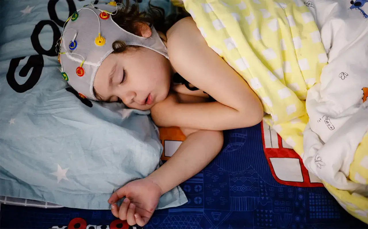 Dziecko śpi w czepku do eeg głowy, z kolorowymi elektrodami.