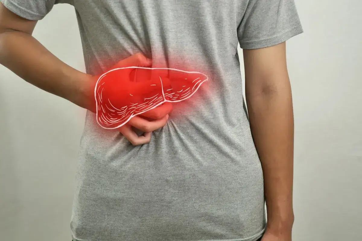 Osoba trzyma się za prawy bok, gdzie widoczna jest czerwona, zarysowana wątroba. Czuje, jak boli wątroba.