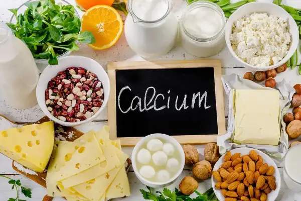 Talerzyk z serem, fasolą, orzechami, migdałami, pomarańczą i nabiałem. Na tablicy napis "Calcium".