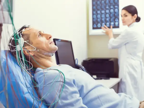 Mężczyzna leży z elektrodami na głowie do badania eeg. Lekarka analizuje wyniki na ekranie.