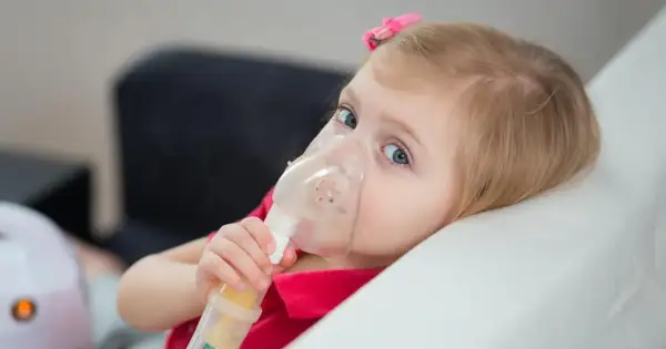 Mała dziewczynka z niebieskimi oczami korzysta z nebulizatora, co jest częścią leczenia mukowiscydozy.