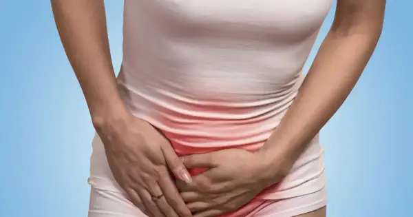 Kobieta trzyma się za brzuch, odczuwając ból w pachwinie. Czerwony obszar na jej ubraniu sugeruje dyskomfort.